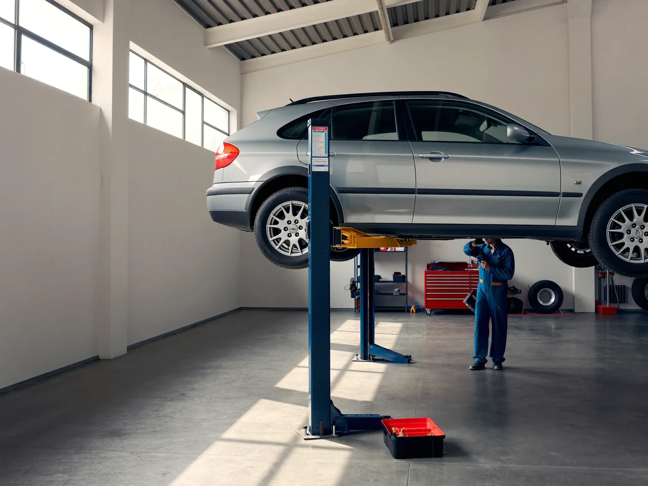 Illustrazione di un'officina luminosa con un'auto sul ponte sollevatore e un meccanico al lavoro